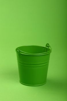 One small green painted metal empty toy bucket over green paper background, close up, high angle view