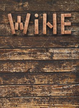 Word WINE shaped by natural wooden wine bottle corks of different vintage years over background of dark old wooden planks