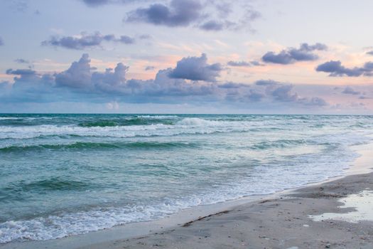 Sea coastal waves rolling on empty sandy beach, stormy cloudy sunrise skyview