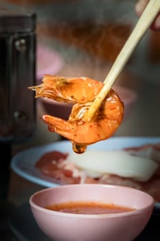 chopsticks holding a prawn with spicy chili sauce