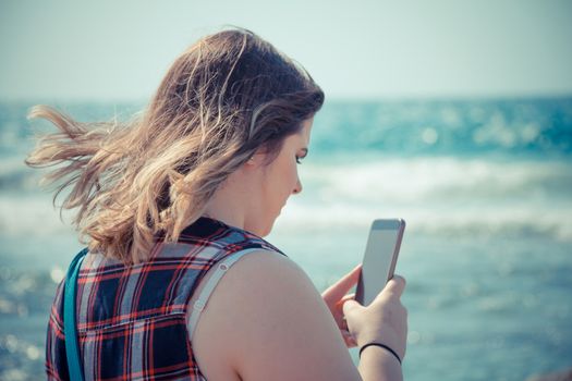 Woman using her smartphone outdoors at the beach near the sea.