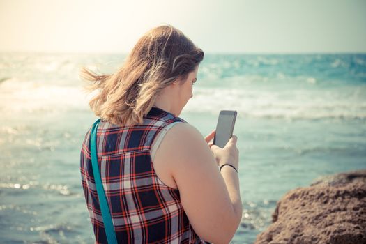 Woman using her smartphone outdoors at the beach near the sea.