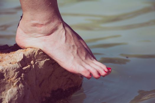Water dripping from caucasian woman bare feet on a rock edge at the river.