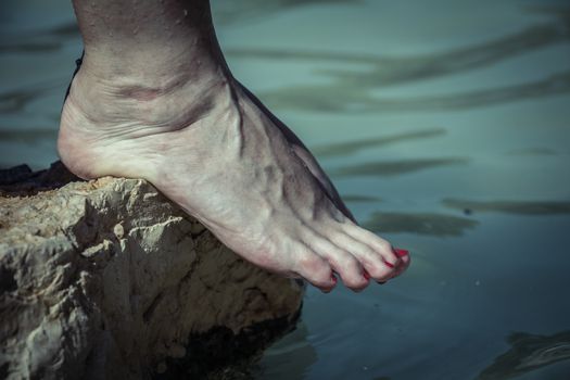 Water dripping from caucasian woman bare feet on a rock edge at the river.