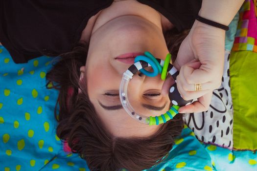 Woman lying on a colorful blanket and looking at camera through a baby toy