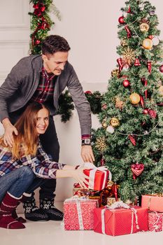Happy parents put christmas gifts for children under decorated tree