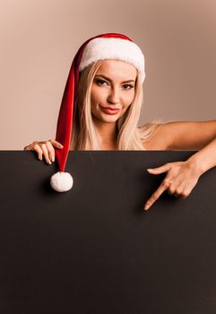 Santa girl holding blank black sign billboard. Christmas woman in Santa hat showing paper sign.