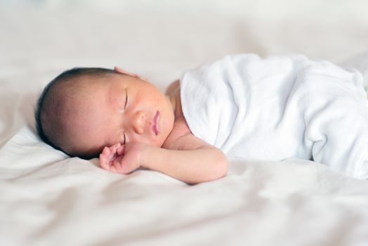 Asian newborn baby boy sleeping in white blanket, 7 days old.