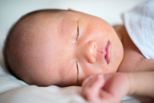 Close up Asian newborn baby boy sleeping in white blanket, 7 days old.
