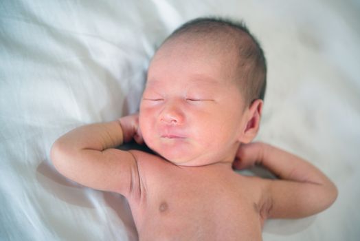 Newborn baby boy lies on bed and stretches, 7 days old.