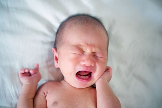 Beautiful newborn baby lying in his bed and crying.