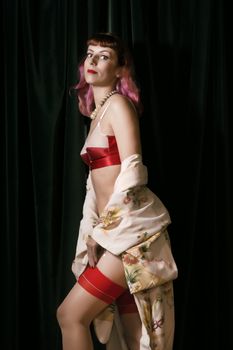 Girl with red vintage lingerie and kimono next to velvet curtains.