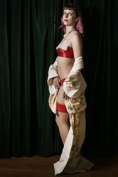 Girl with red vintage lingerie and kimono next to velvet curtains.