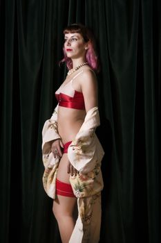 Girl with red vintage lingerie and kimono next to velvet curtains.