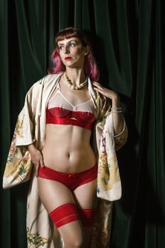 Girl with red vintage lingerie and kimono next to velvet curtains.