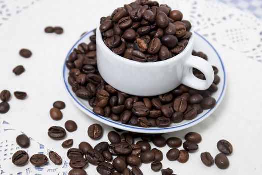 Composition of a cup full of coffee beans on table.