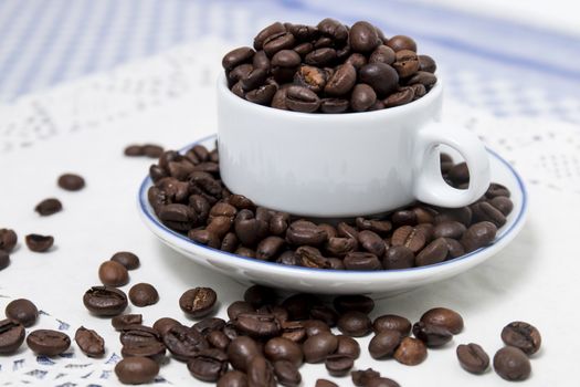 Composition of a cup full of coffee beans on table.