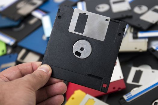 hand grabs a floppy disk from a big pile on the background.