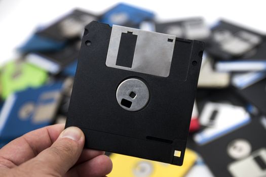 hand grabs a floppy disk from a big pile on the background.