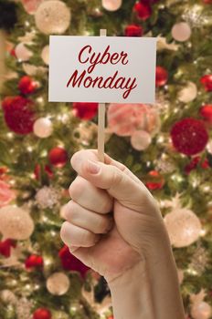 Hand Holding Cyber Monday Card In Front of Decorated Christmas Tree.