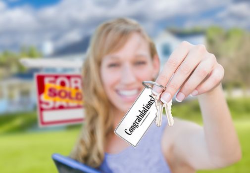 Woman Holding New House Keys with Congratulations Card In Front of Sold Real Estate Sign and Home.