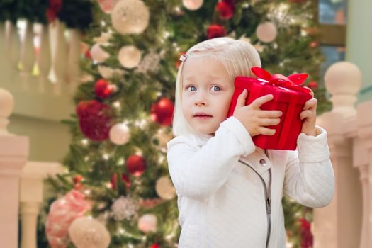 Happy Young Girl Holding Gift Box In Front of Decorated Christmas Tree.