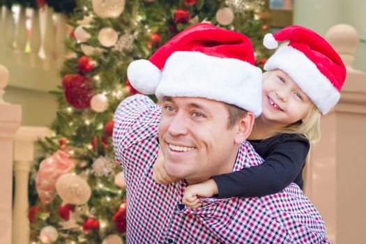 Father and Daughter Wearing Santa Hats In Front of Decorated Christmas Tree.