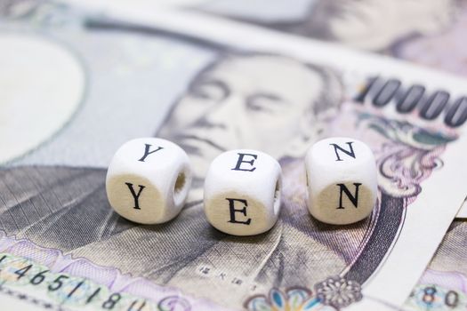 close-up of wooden cube with text "Y E N" on banknote YEN for business and financial concept.