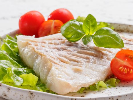 Close up view of grilled codfish with basil and cherry tomatoes in trendy white plate.