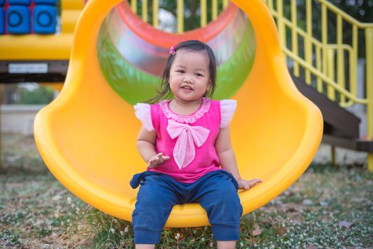 Toddler girl playing on a slide at children playground.