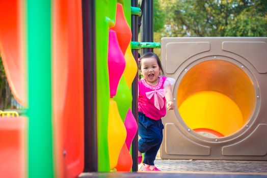 Toddler girl playing on a slide at children playground.