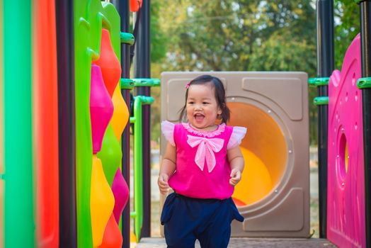 Toddler girl playing on a slide at children playground.