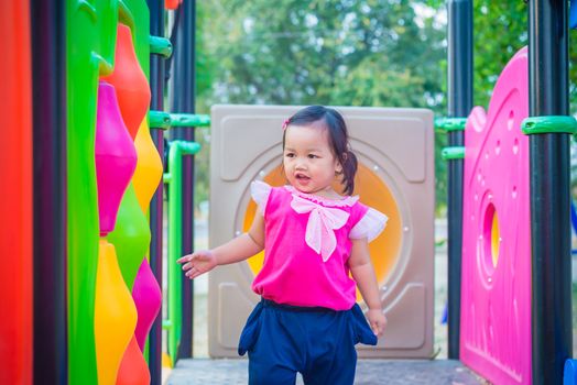 Toddler girl playing on a slide at children playground.