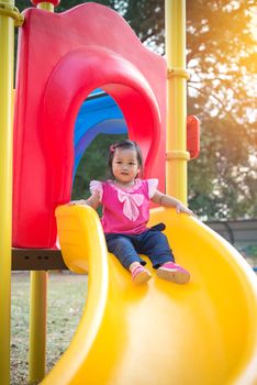 Toddler girl playing on a slide at children playground.