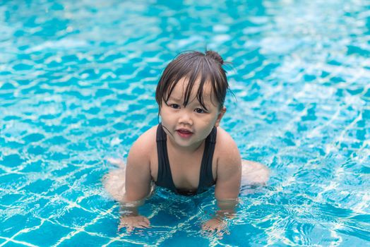 Cute girl or little child playing in swimming pool happily.