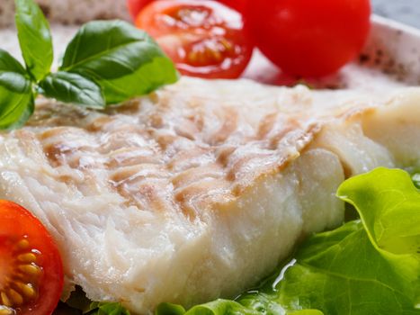 Close up view of grilled codfish with basil and cherry tomatoes in trendy white plate.