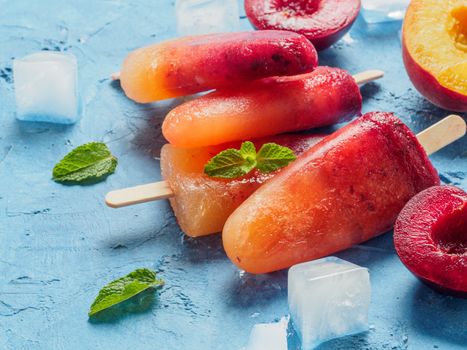 Close up view of plum and peach popsicle on blue concrete background. Fruit popsicles ice cream with fresh plums and peach. Copy space.