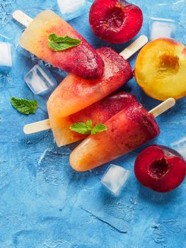 Close up view of plum and peach popsicle on blue concrete background. Fruit popsicles ice cream with fresh plums and peach. Copy space.