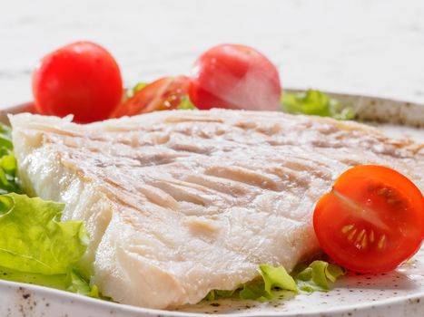 Close up view of hot grilled codfish with basil and cherry tomatoes in trendy white plate.