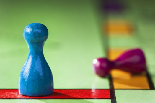 Close up of a blue pawn winner and a purple pawn loser on a board game with selective focus
