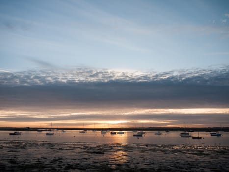 sun set sky dramatic clouds sea front beach harbor marina boats moored landscape; west mersea, essex, england, uk