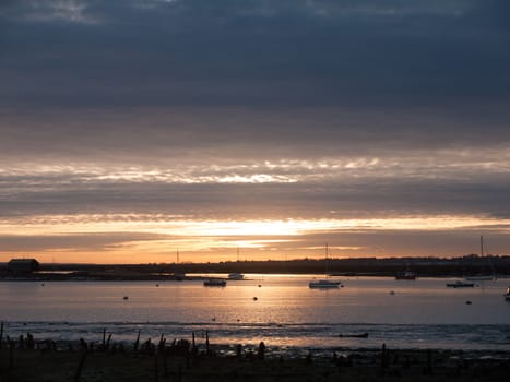 sun set sky dramatic clouds sea front beach harbor marina boats moored landscape; west mersea, essex, england, uk
