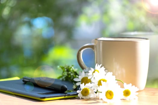 Mug, daisies, graphics tablet. The concept of am designer. A Sunny summer morning.