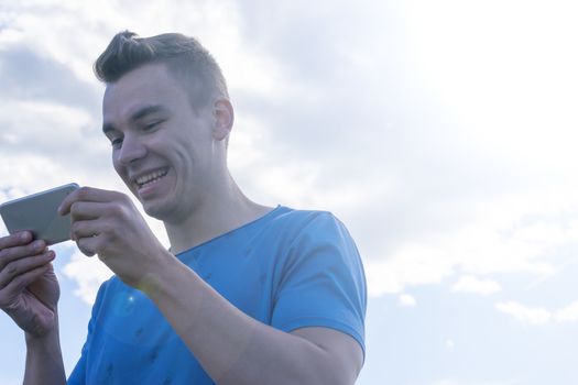 A young man emotionally looks at the phone. Nature, summer, portrait.