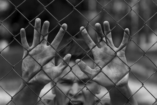 A young man behind bars. Imprisonment, famine, war.