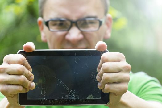Young man in glasses holding broken tablet PC at arm's length.