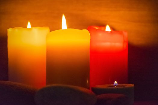 Several multi-colored candles are lit and surrounded by stones.