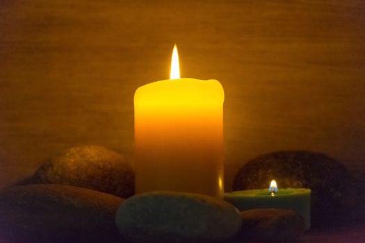 Several multi-colored candles are lit and surrounded by stones.