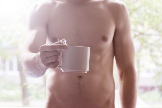A young man holding a mug in his hands. Morning, summer, autumn, bare-chested. Tea, coffee.