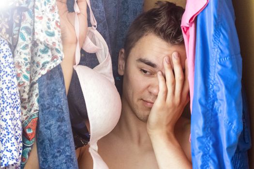 A young man hiding in the closet among women's clothing. Lover in the closet.